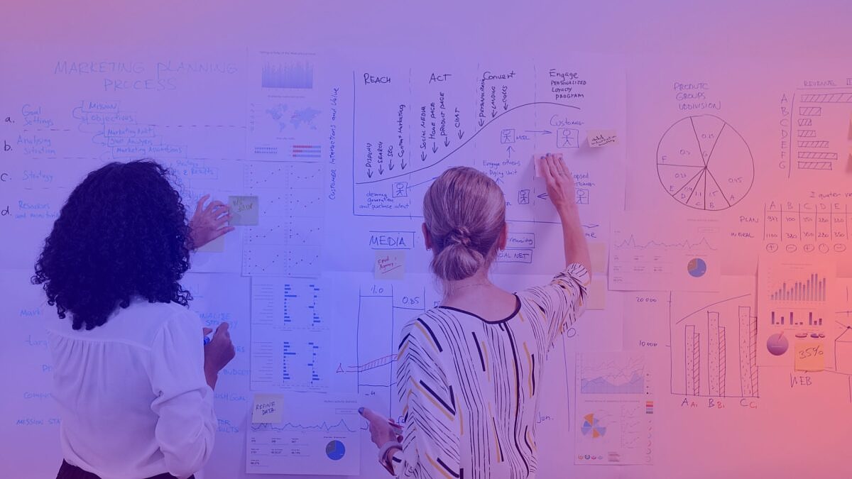 Zwei Marketingexpertinnen analysieren Strategien und Daten an einer Wand mit Diagrammen und Charts zum Thema Nachhaltigkeitskommunikation