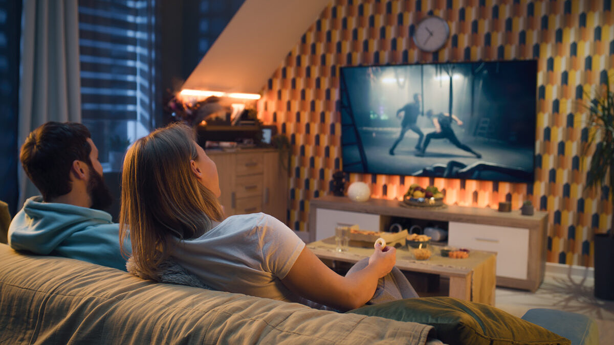 CTV advertising: A man and a woman are sitting on the sofa in their living room watching an advertising clip on TV.
