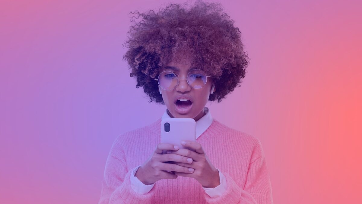 Junge Frau mit lockigem Haar und Brille schaut auf ihr Smartphone – Symbolbild für LinkedIn-Beiträge, die ohne unsere Tipps schnell cringe wirken.