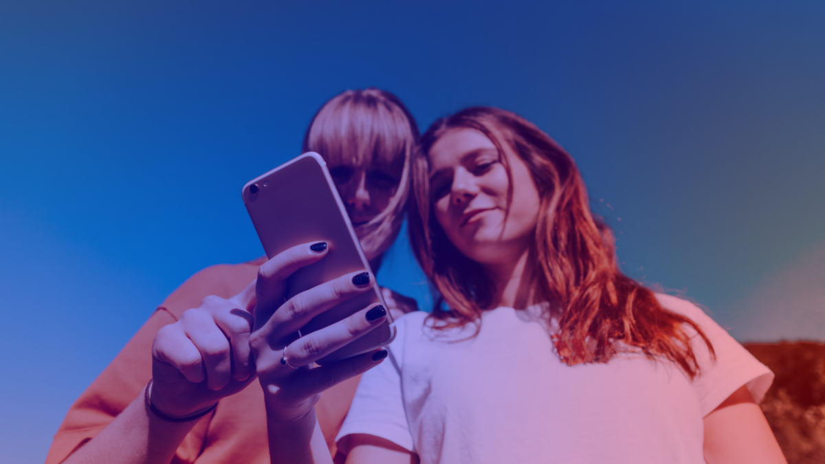 Two young people look at a smartphone – the content they view is dictated by AI search visibility.